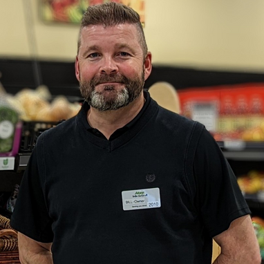 Middle aged man wearing a black golf shirt. He has light brown hair and a grey and brown beard.