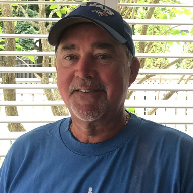Middle aged man wearing a light blue t-shirt and dark blue baseball hat.
