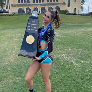 Young girl with brown hair in a pony tail. She is wearing a black and blue cheerleading uniform and holding a trophy.