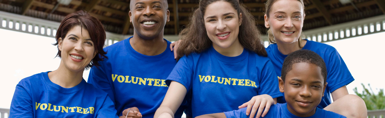 A group of five diverse volunteers wearing bright blue t-shirts that say 'Volunteer'.