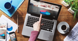 A laptop displaying financial statements on a table with a coffee up, cell phone and printed financial statements.